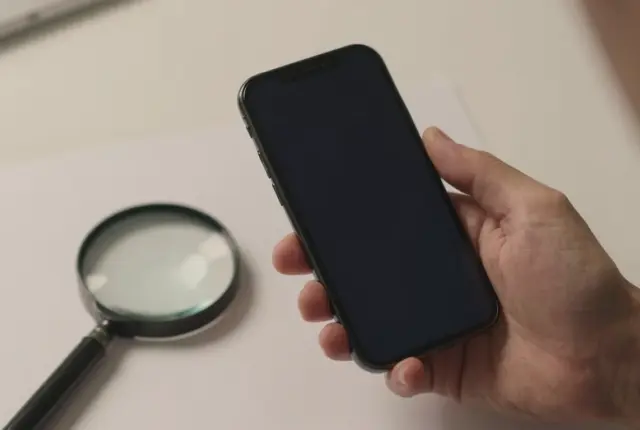 A smartphone inspected closely beside a glass magnifier on a plain desk